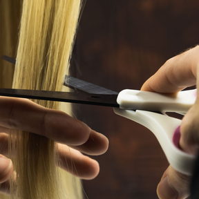 Shears closing on a section of hair lifted over a comb. Only the hands, the hair and the tools are in frame.