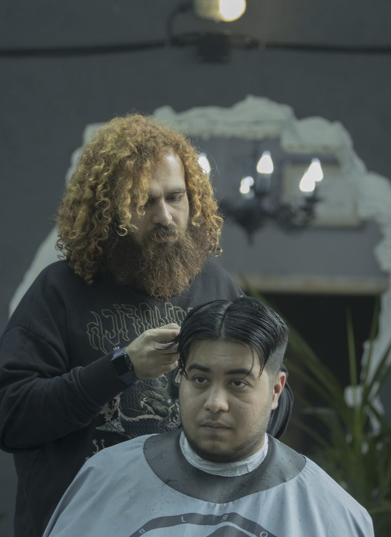 A barber combing through a caped customer's hair before cutting.