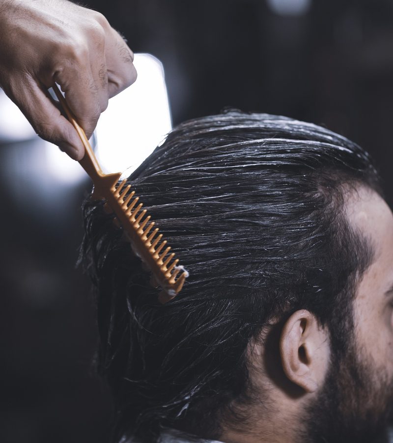 A comb drawn back through slicked hair during a barbering appointment.