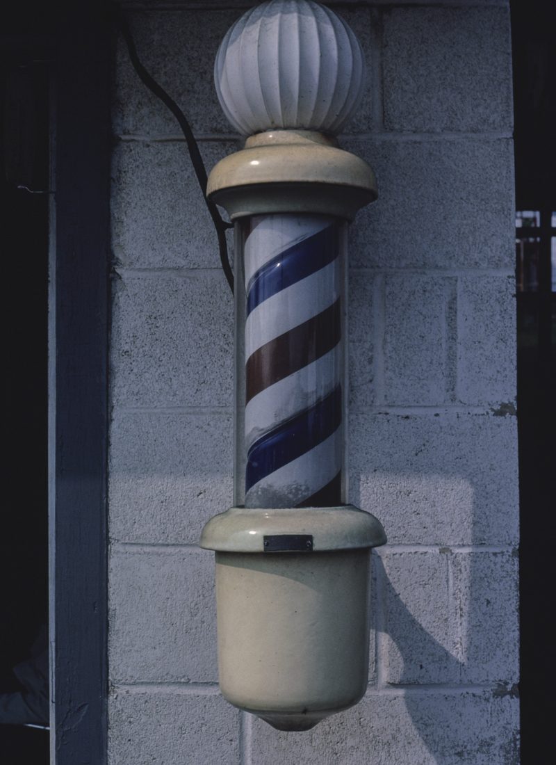 A barber pole fixed to a painted cinder-block wall.