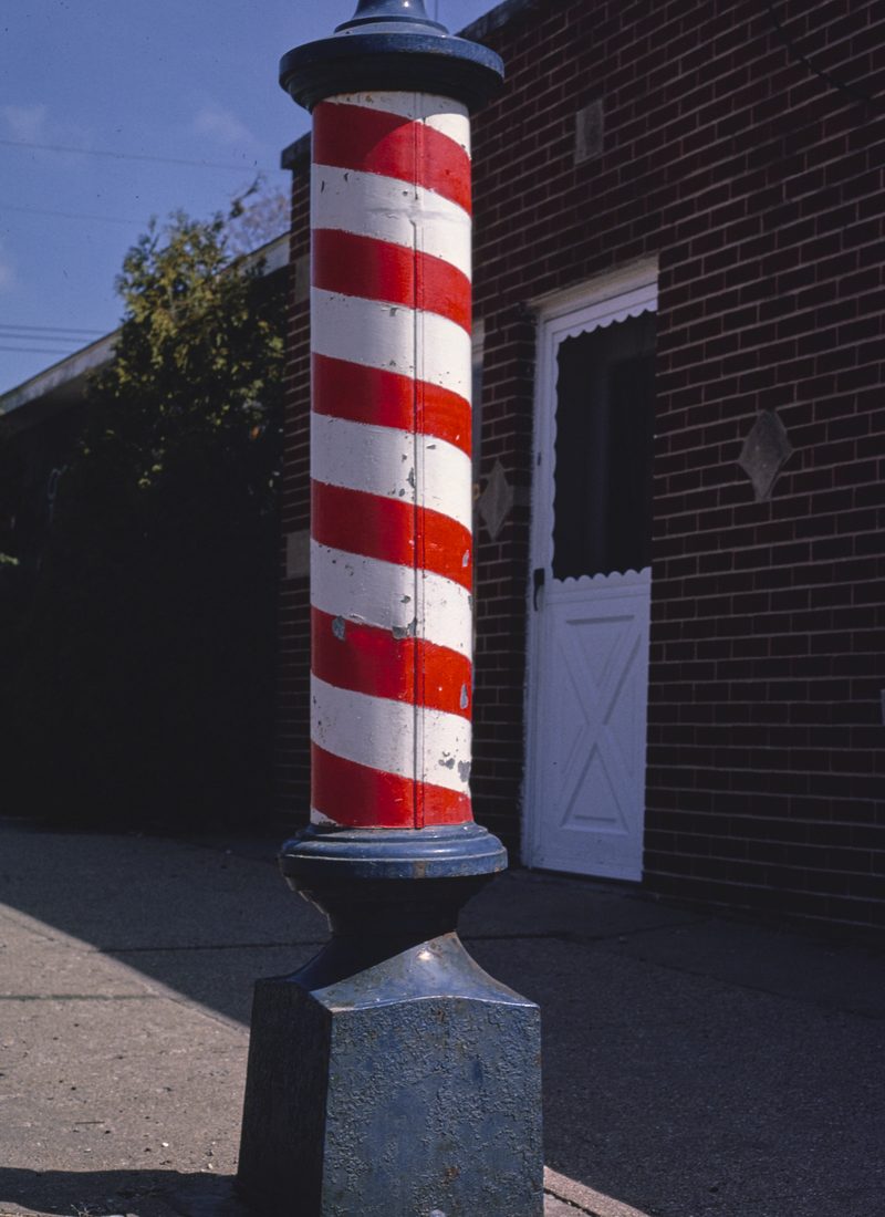 A red, white and blue barber pole mounted on a brick wall.