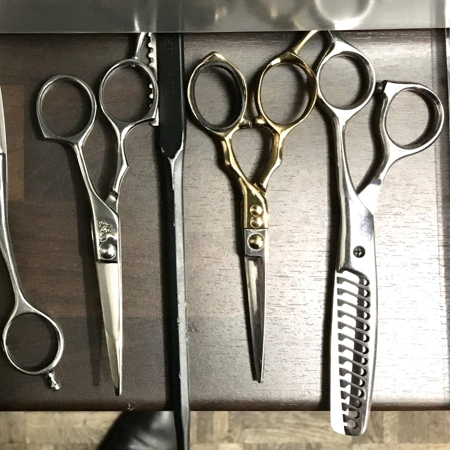 Several pairs of haircutting scissors arranged on a dark wooden rack.