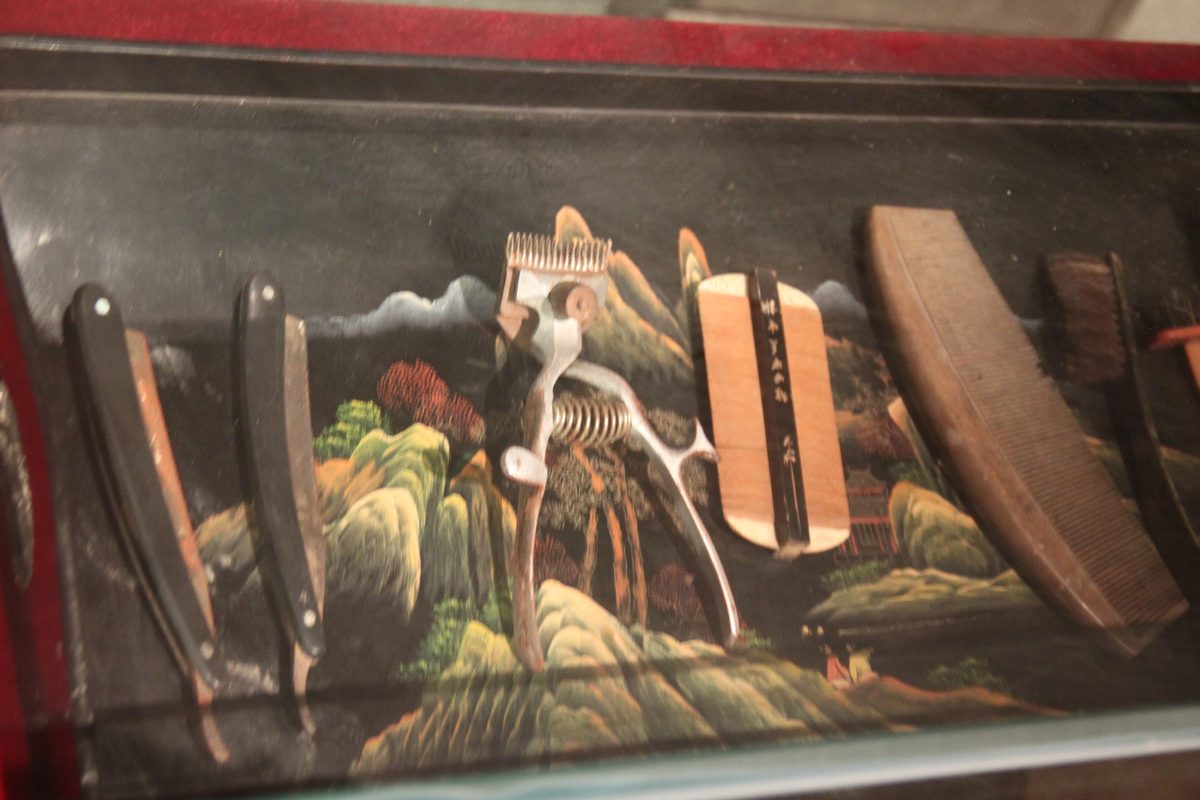 A set of old barber's hand tools laid out inside a glass display case.