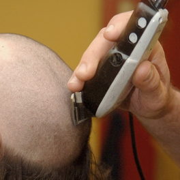 Shop detail: a hand runs clippers over the crown of a client's head.