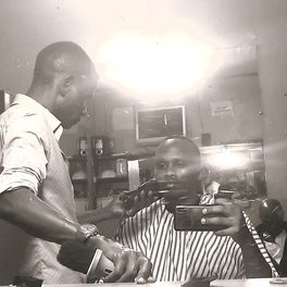 Shop detail: a barber trims a customer's beard, seen in the mirror.