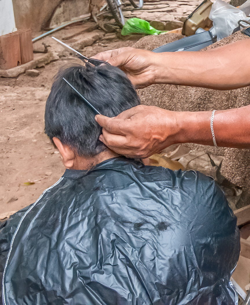 A barber works with scissors at the back of a caped client's head. The face is out of frame.