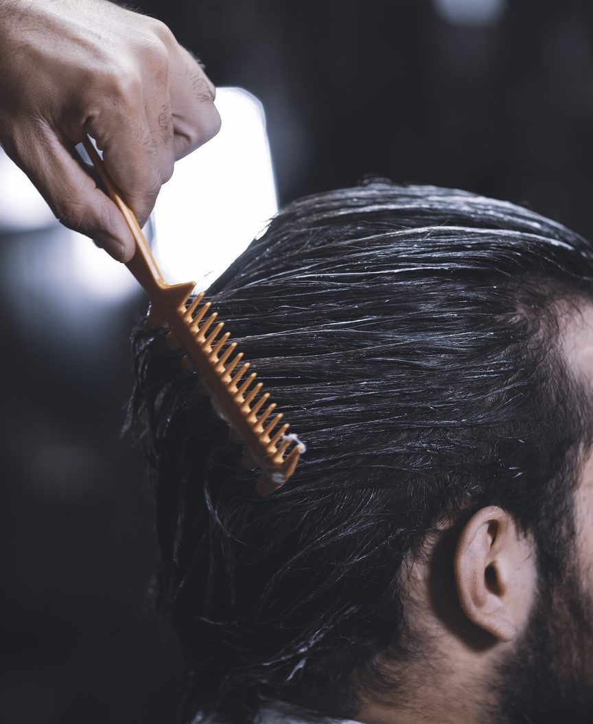 A comb drawn back through slicked hair at the chair. No face is in frame.