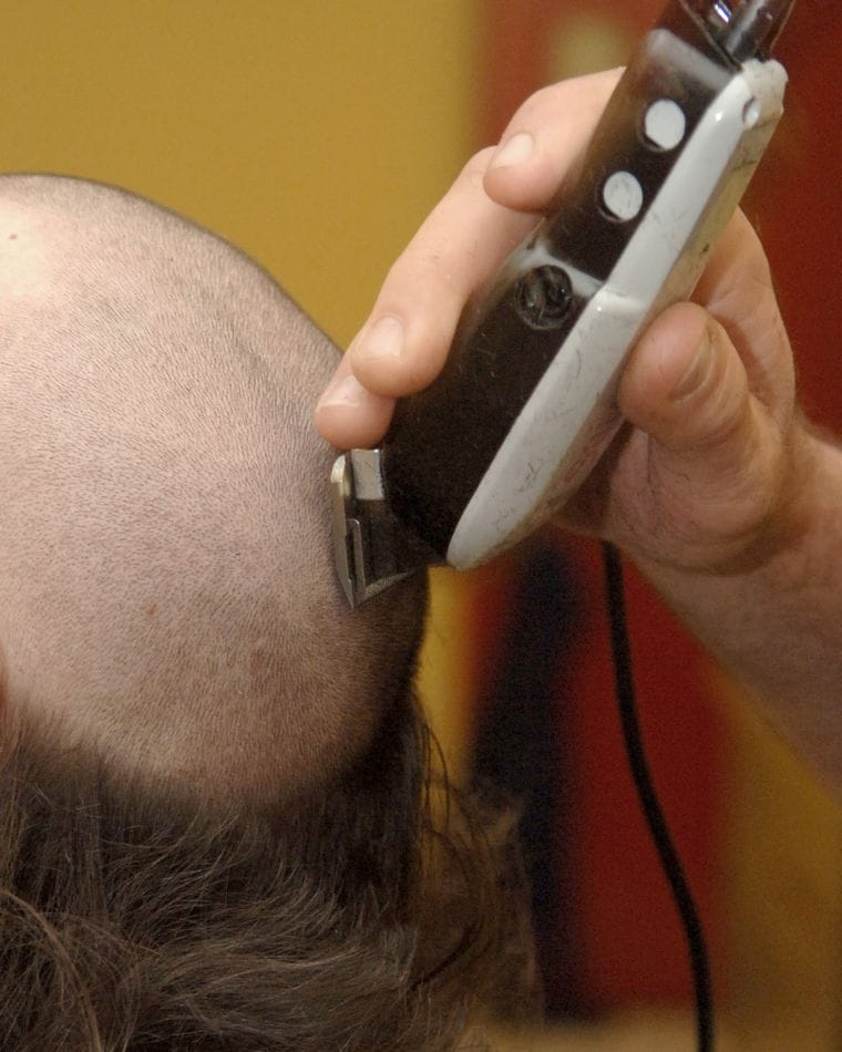 A barber's hand running an electric clipper up the back of a client's head, close to the skin.