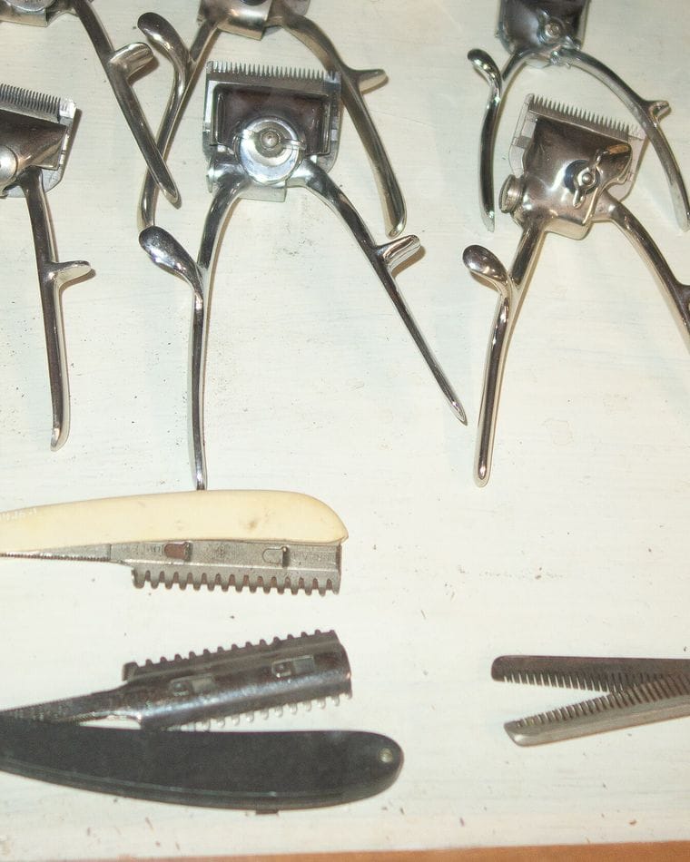 Antique hand-operated hair clippers and spare toothed blades laid out on a pale cloth.