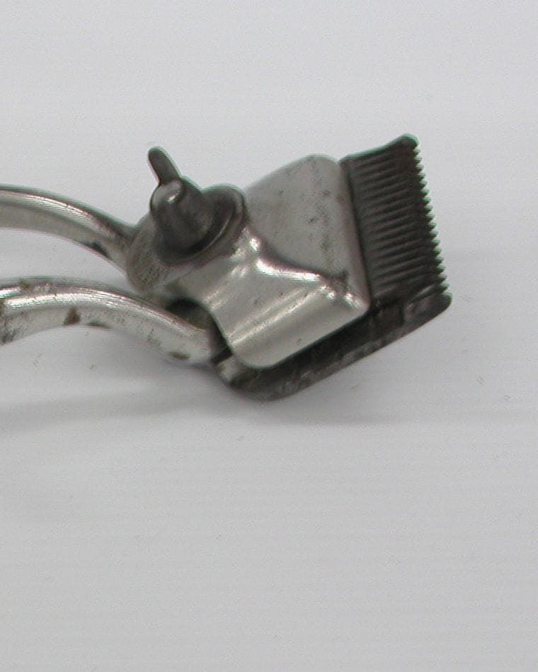 A close view of an antique metal hand clipper with a toothed cutting head, on a white surface.