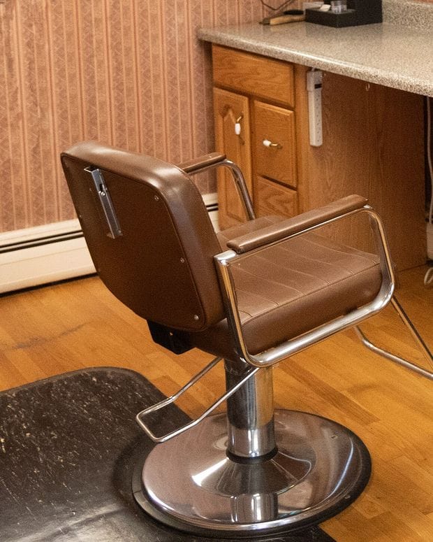 An empty brown barber chair turned towards a cutting station counter on a wooden floor.