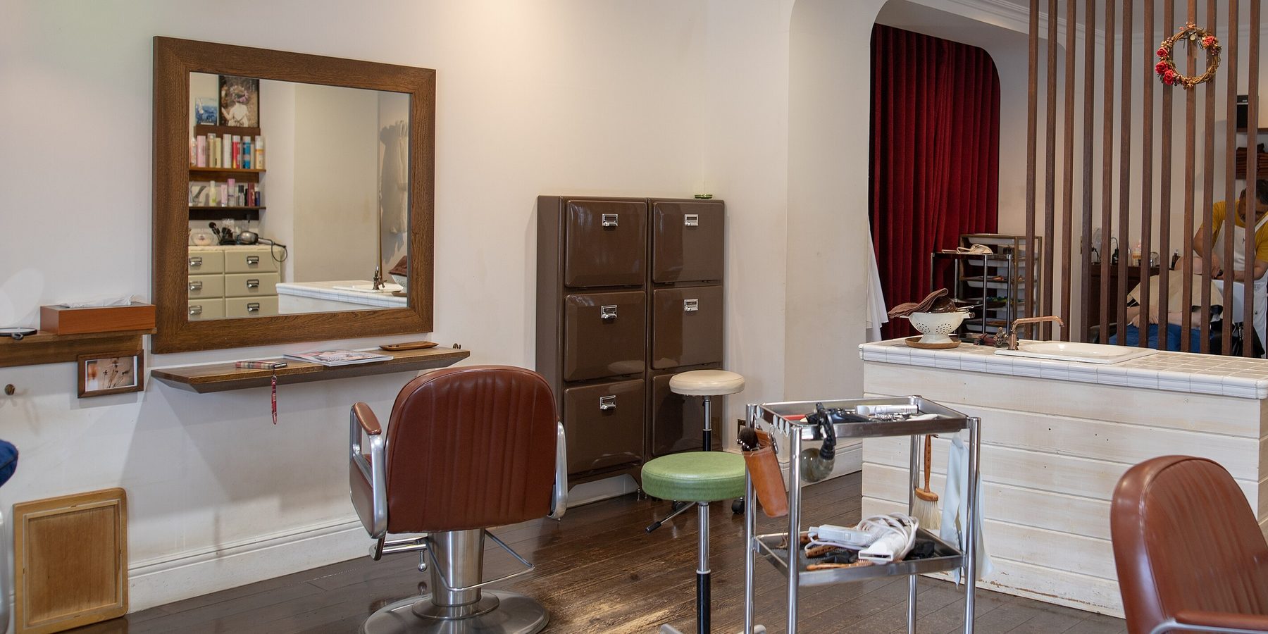 A single barber chair facing a wall mirror, with a tool trolley and wash counter beside it
