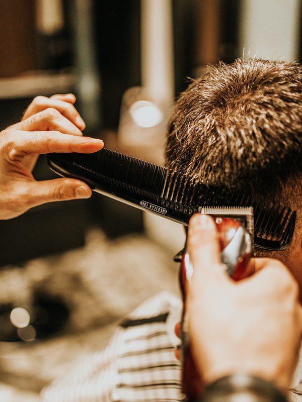 A barber blending the back of a client’s neck with comb and clipper