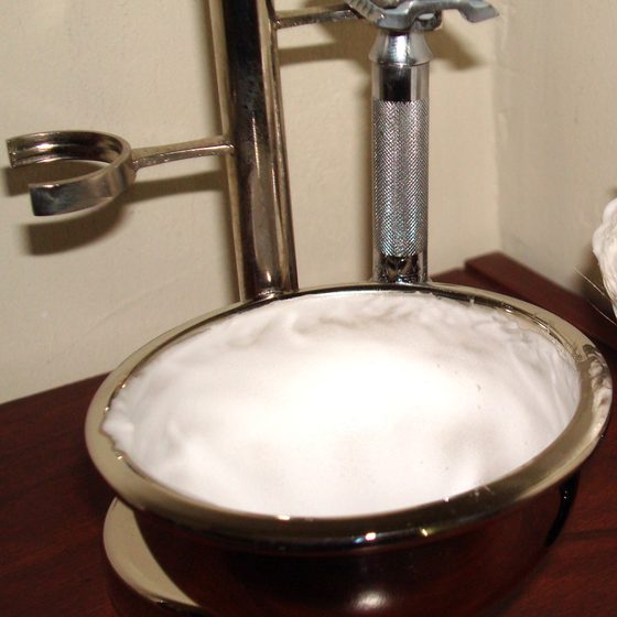 A shaving bowl of fresh lather beside a safety razor on its stand
