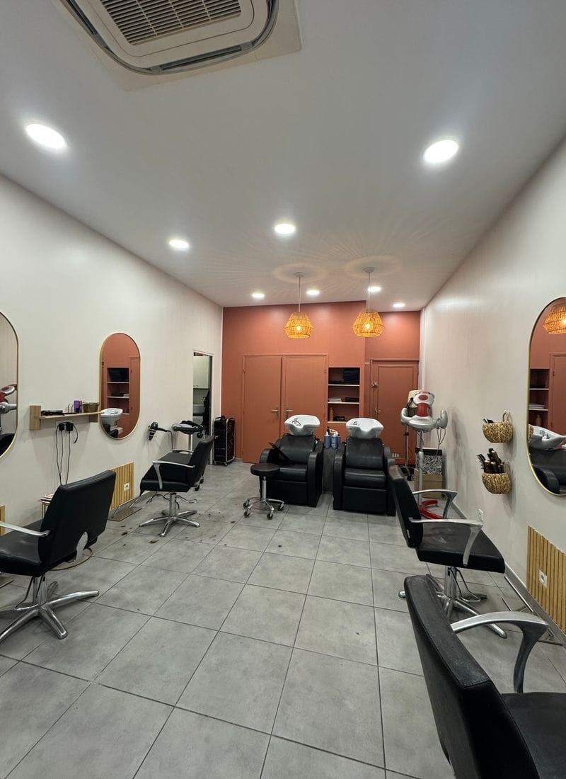 A bright salon floor with styling chairs, round mirrors, a wooden reception counter and basins at the back.