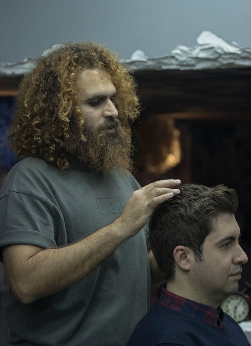 A stylist shaping a seated client's hair with his fingers and a comb before cutting.