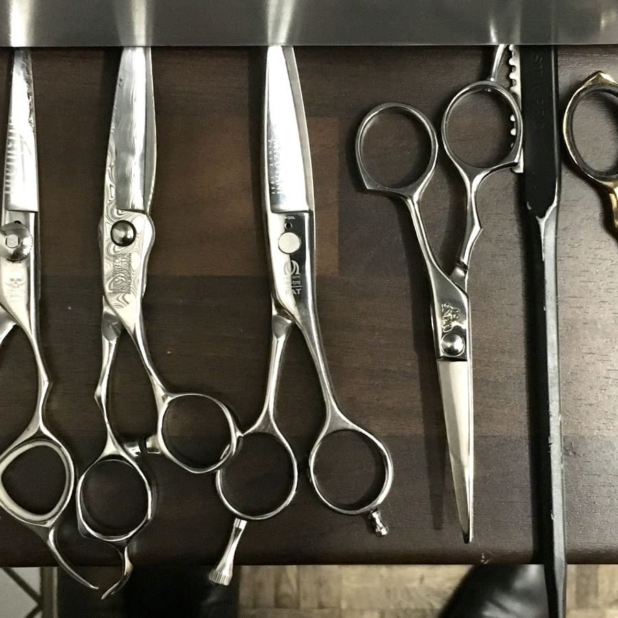Several pairs of haircutting scissors arranged on a dark wooden rack.
