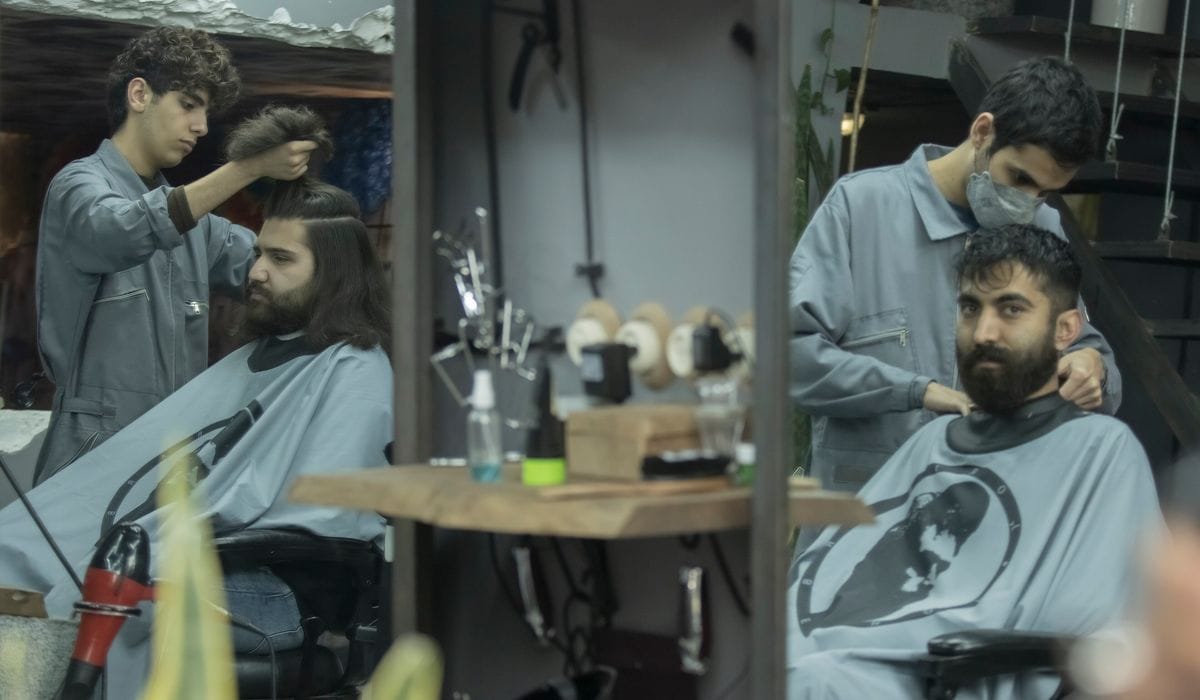 Two stylists cutting at neighbouring stations, each client caped, reflected in the mirrors.