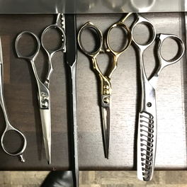 Salon detail: the end of a rack of haircutting shears, a gold-handled pair beside a thinning pair.