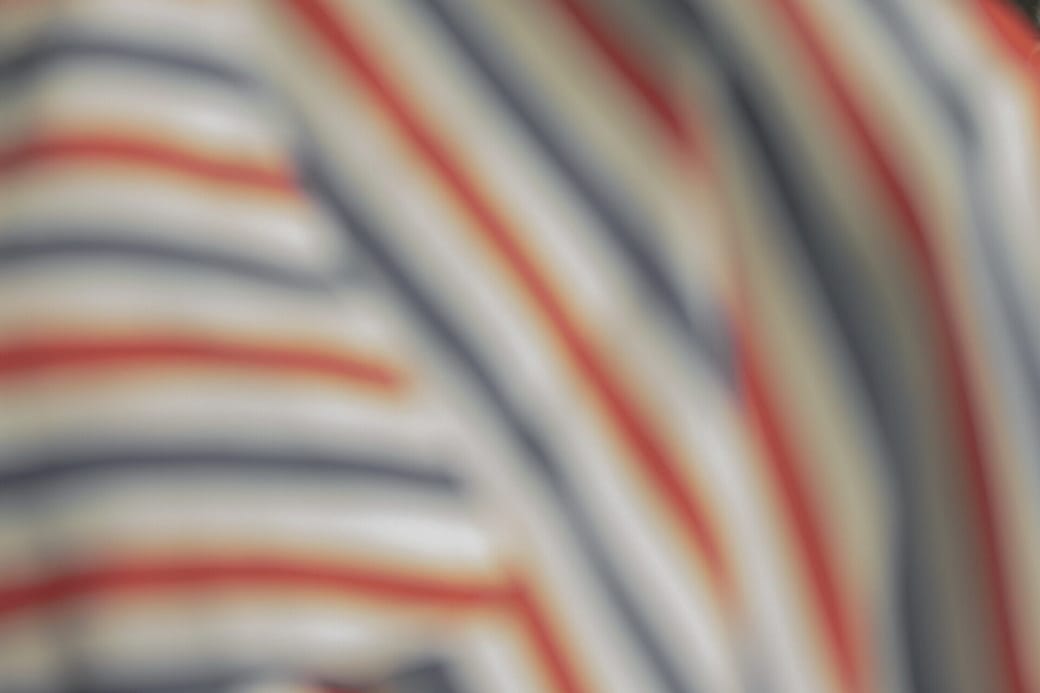The back of a salon guest beneath a striped cutting cape, with the room softly out of focus.