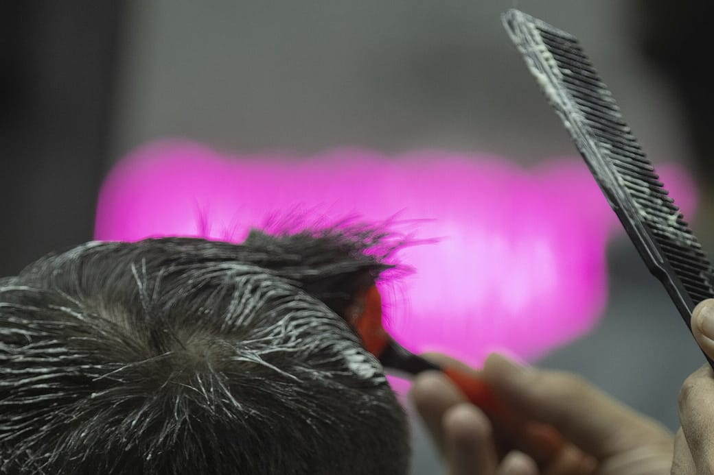 The back of sectioned dark hair with a comb and anonymous hands working close to the crown.