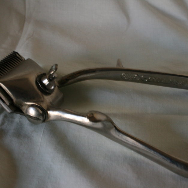 A chrome hand-powered clipper lying on white cloth, its blades catching the light.