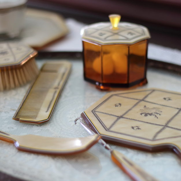 An unbranded hairbrush, comb, hand mirror and amber jar set out together on a tray.