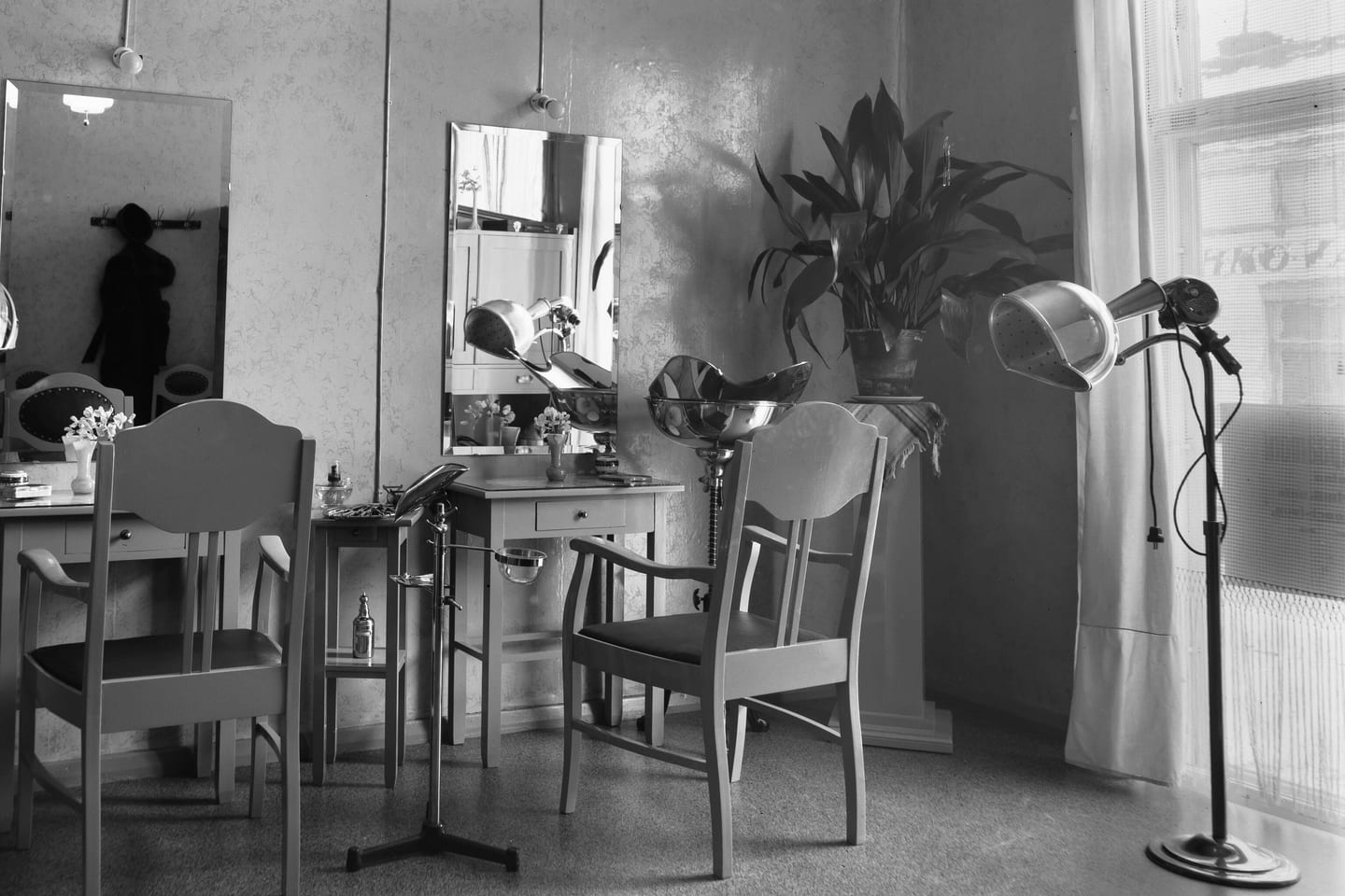 A black and white photograph of a salon in 1934, with a dressing table, a mirror and a hood dryer on a stand.