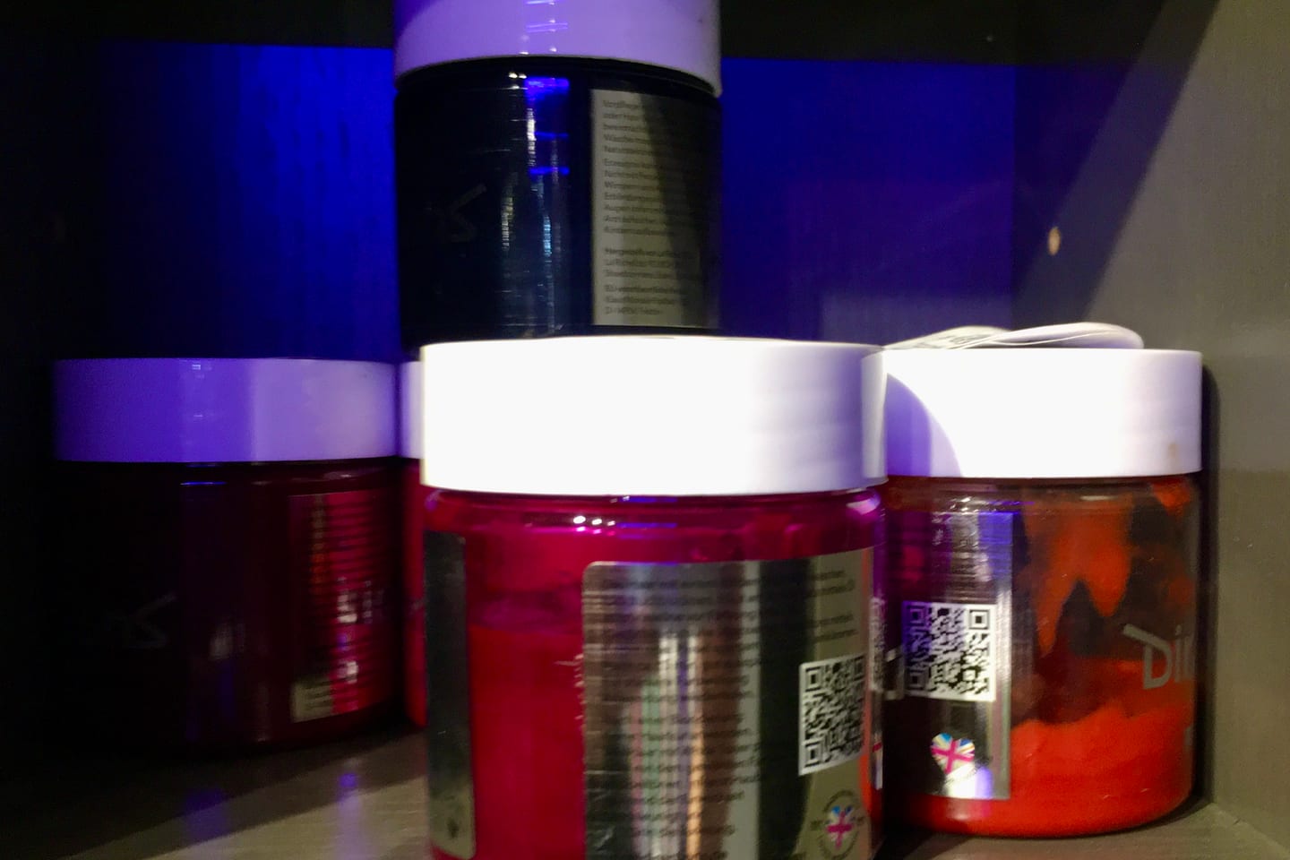 Jars of semi-permanent hair colour lined up on a lit shelf.