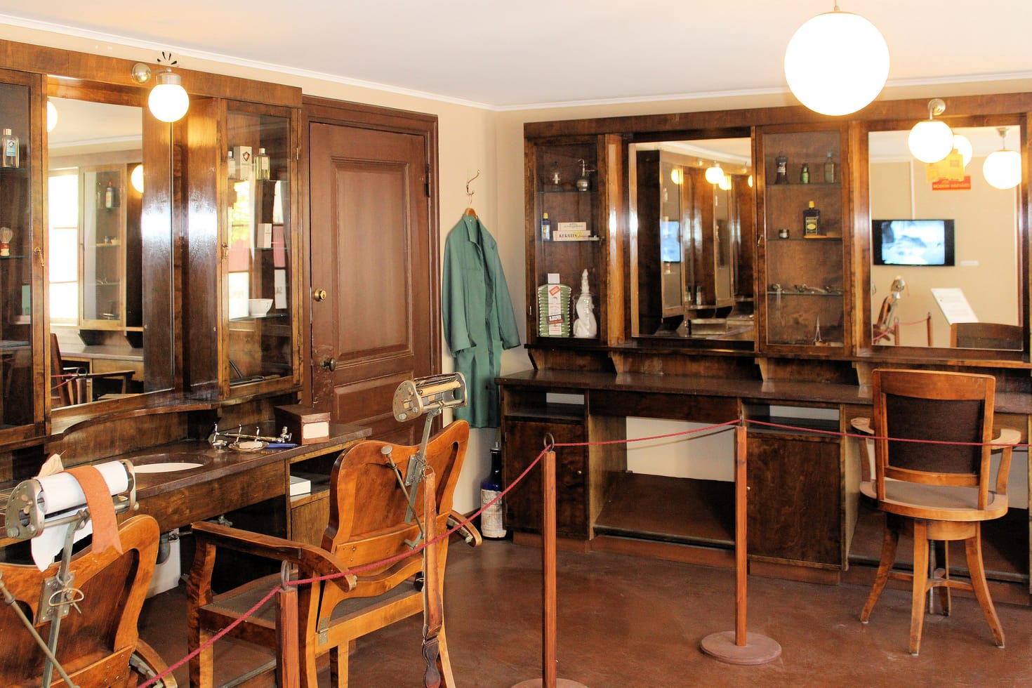 A preserved hairdressing salon at an open-air museum, with an old styling chair in front of a mirror.