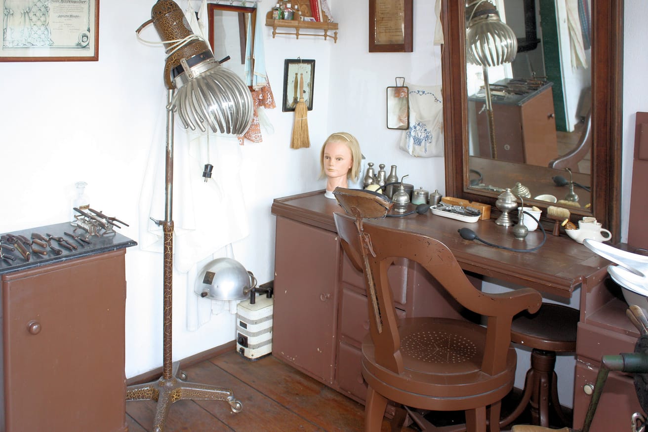 A reconstructed village hairdresser's shop with a styling chair facing a mirror.