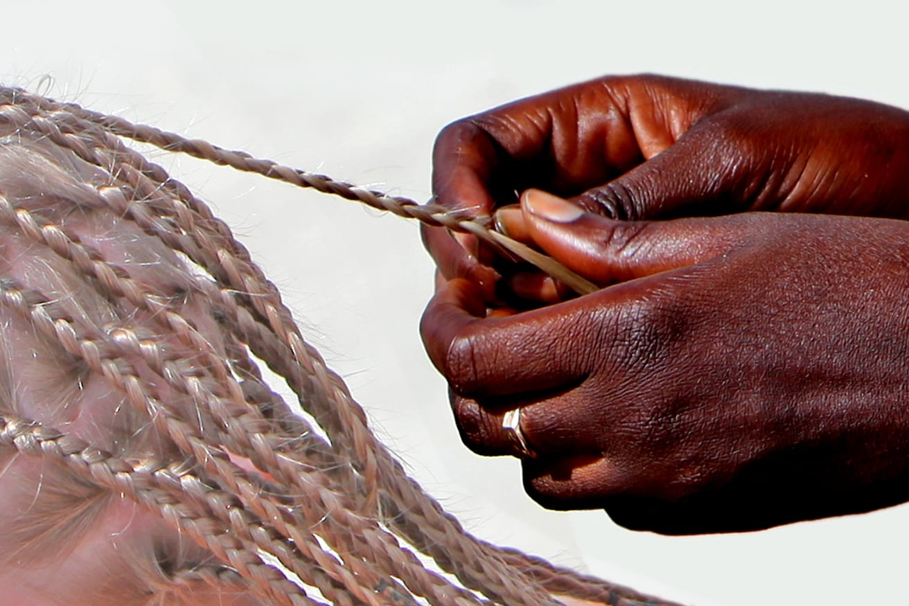 Hands braiding a section of long hair into narrow plaits.