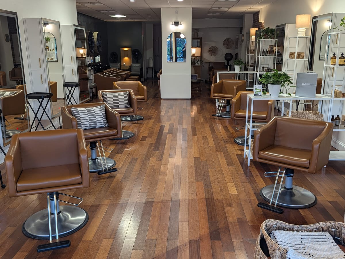 The inside of a hair salon, with styling chairs set in front of a long run of mirrors and nobody in the chairs.