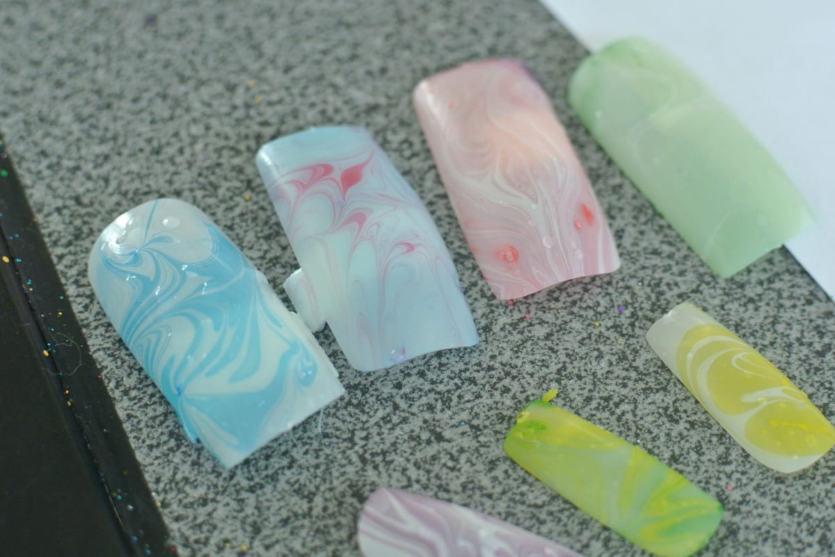 Hand-painted false nails laid out on a work mat, marbled in pink, white and gold.