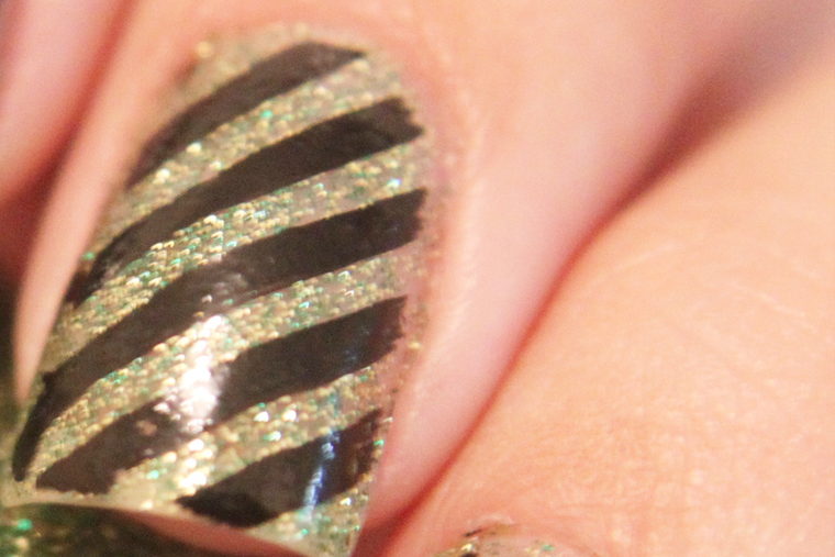 A close view of one nail in gold glitter, striped diagonally in black.