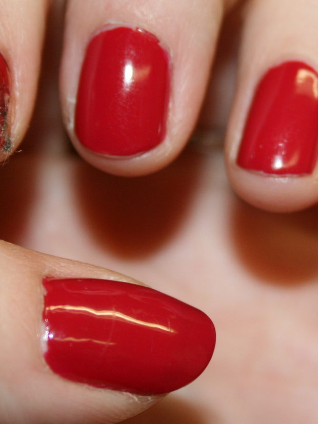 A close view of three nails in a deep red cream polish, the hand at rest.