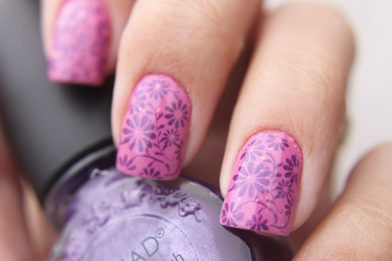 Pink nails stamped with a small purple flower pattern, with a bottle of lilac polish behind them.