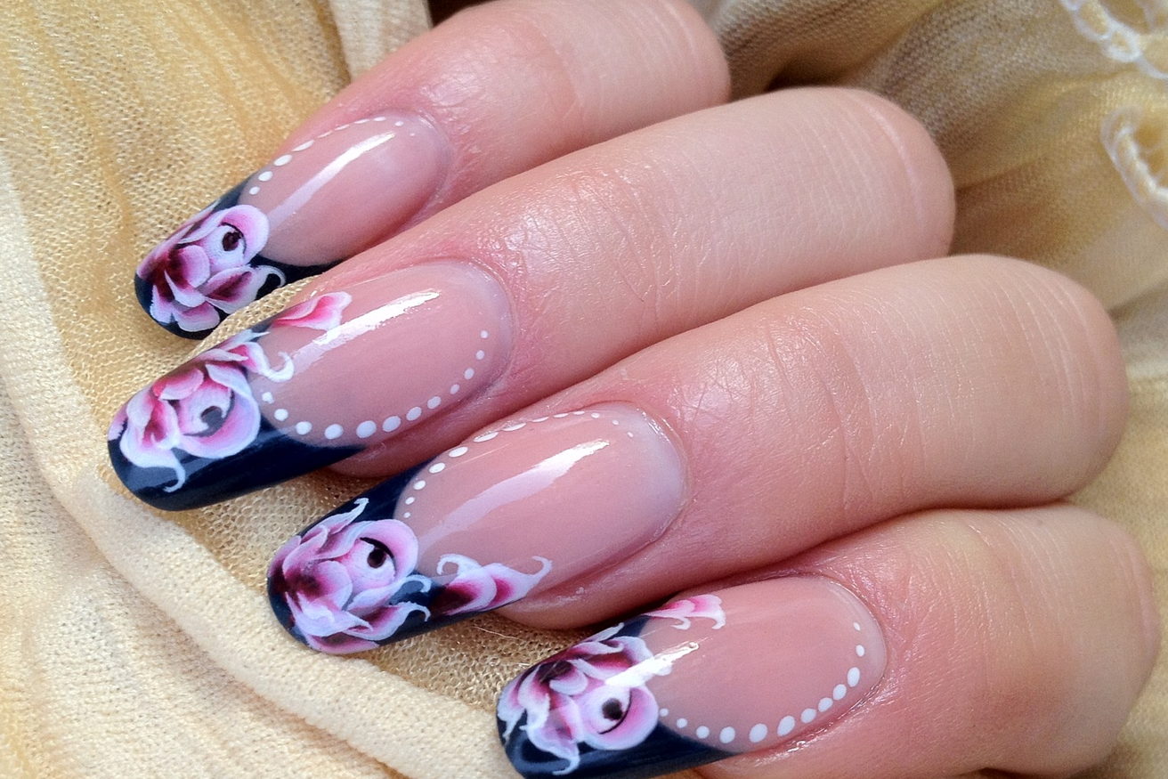 A hand with long square nails, navy tips hand-painted with pink roses and a dotted edge.