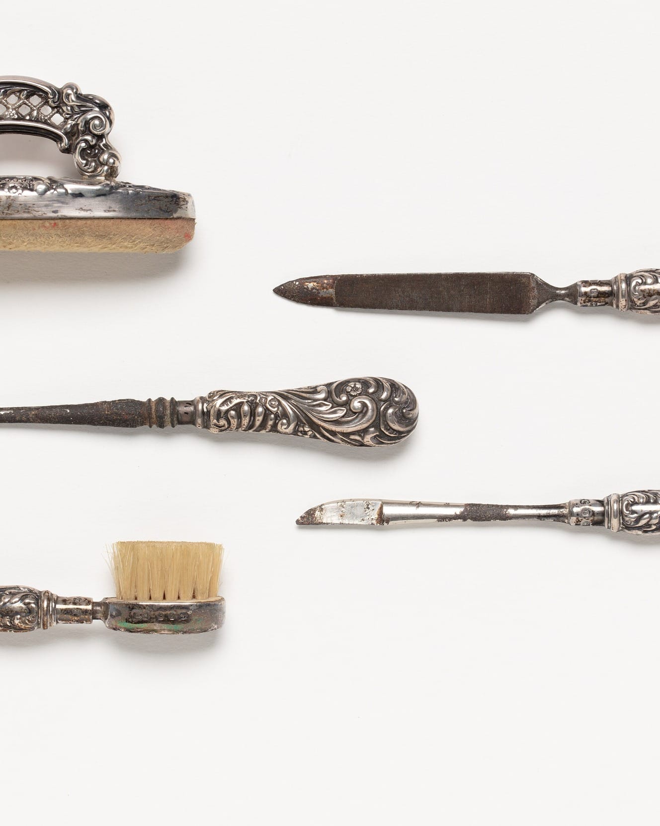 Antique manicure tools with ornate silver handles laid out on a white background.