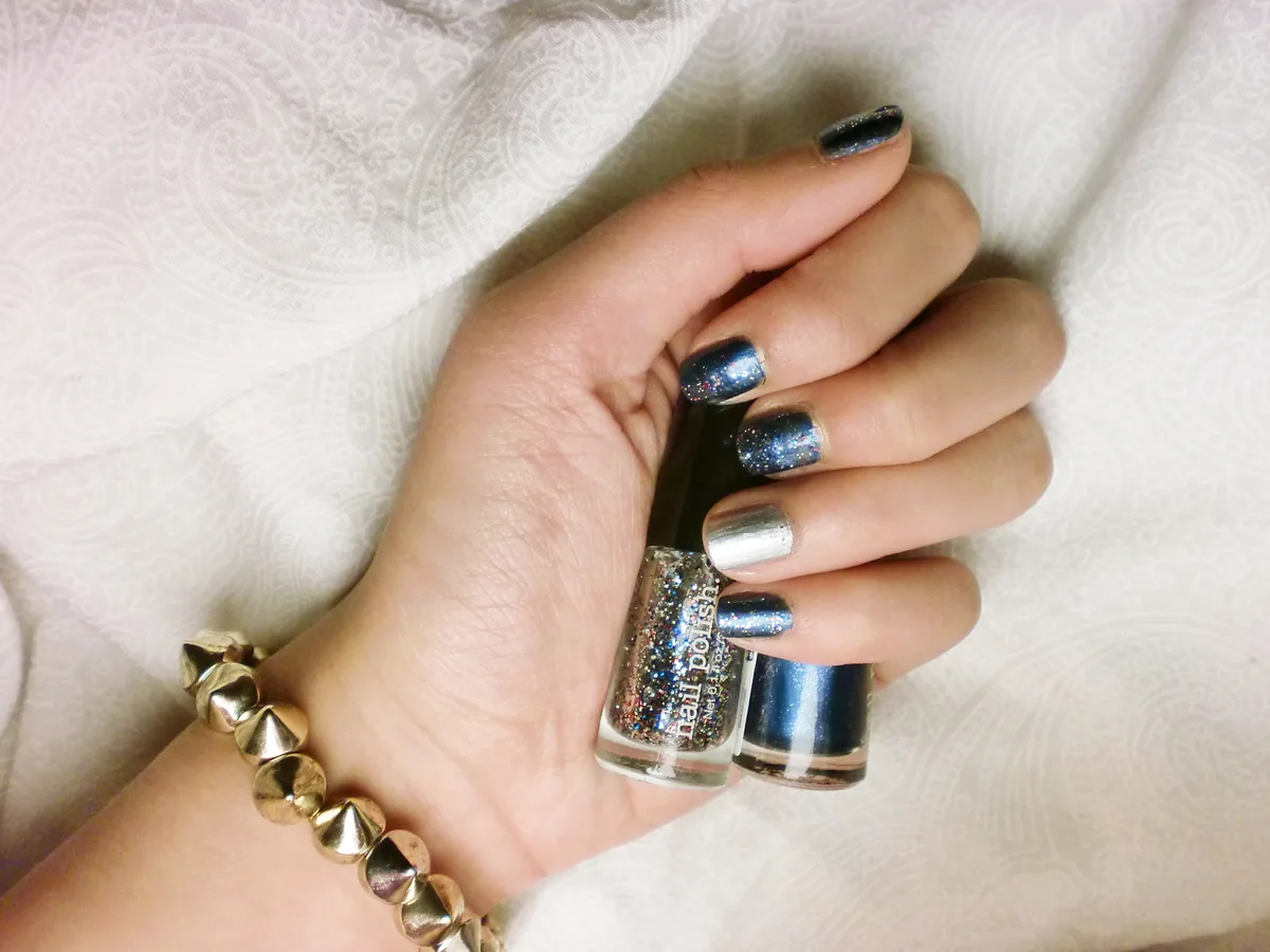 Hand with glitter and chrome nails holding two polish bottles