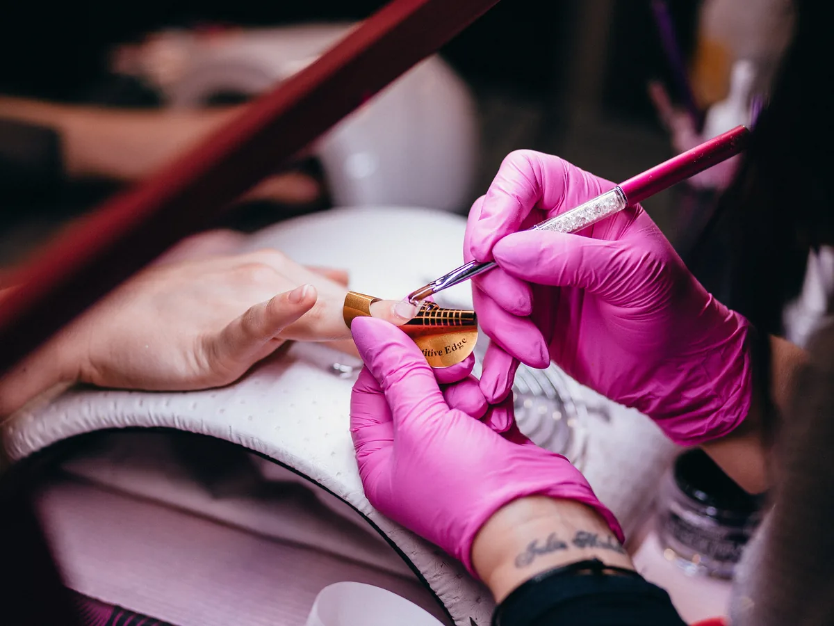 Nail technician in gloves painting a nail with a fine brush