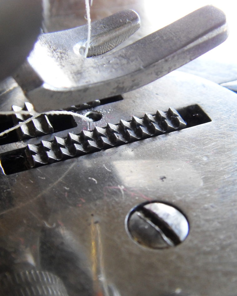 Extreme close view of the feed dogs and presser foot of a sewing machine.