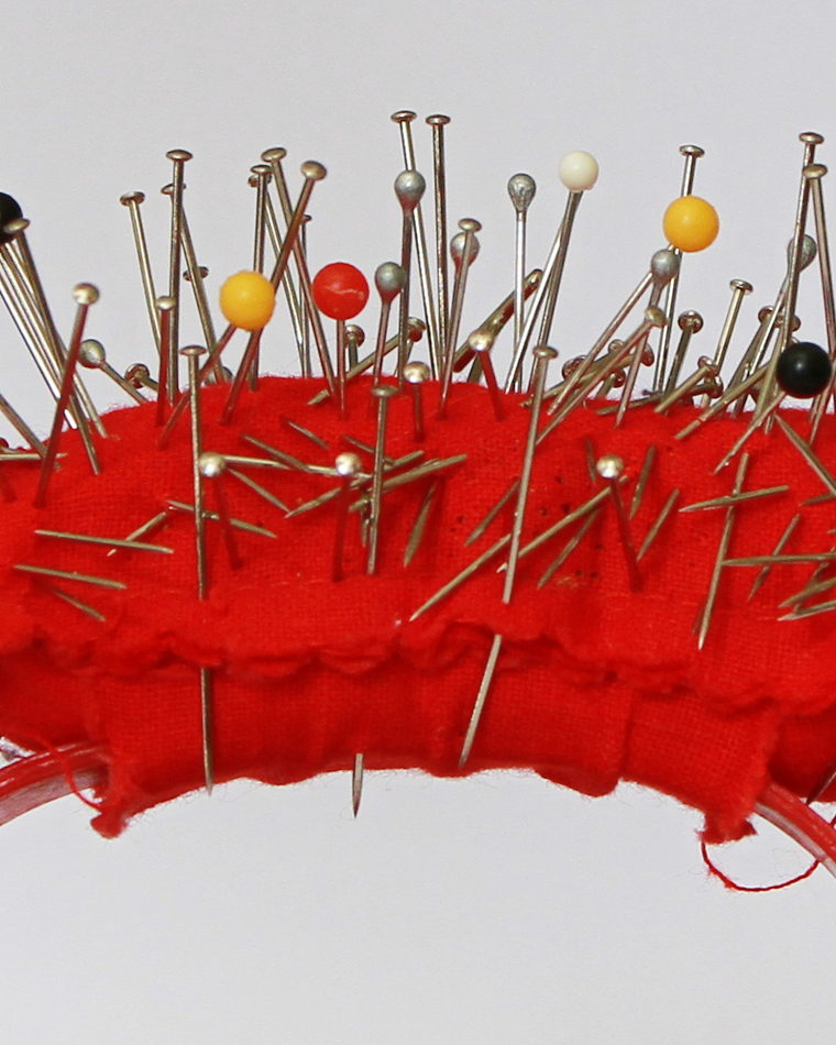 A tomato-shaped pincushion holding dressmaking pins with coloured glass heads.