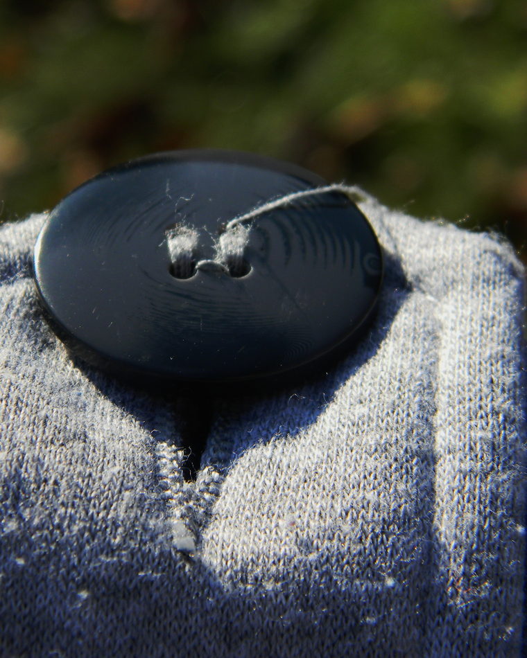 A single blue four-hole button sewn onto blue cloth, photographed closely.