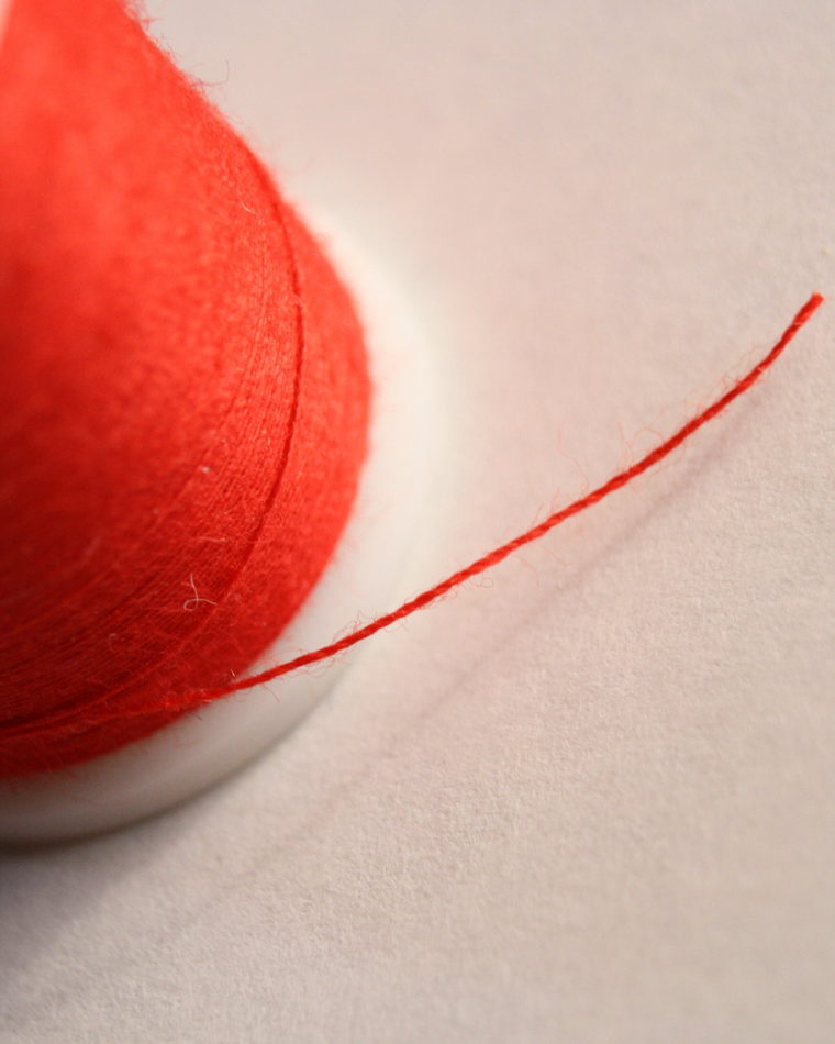 A wooden spool wound with red thread, standing on a plain surface.