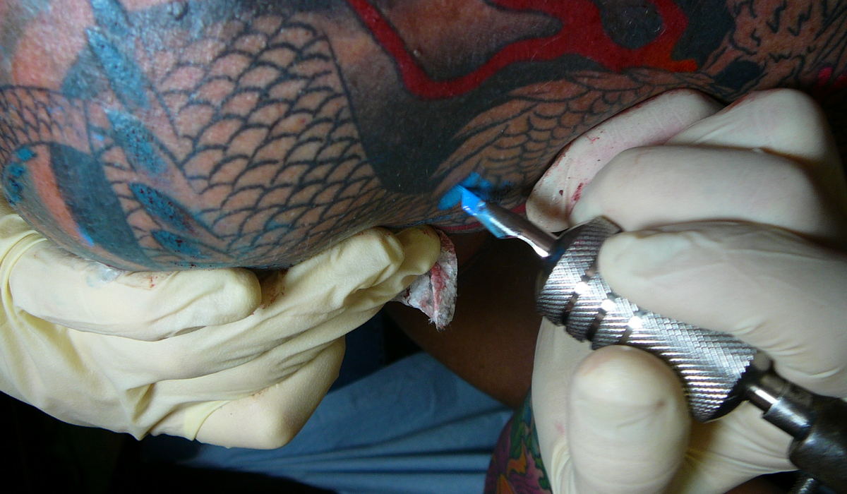 Gloved hands working on a finished back piece, the machine held like a pen.