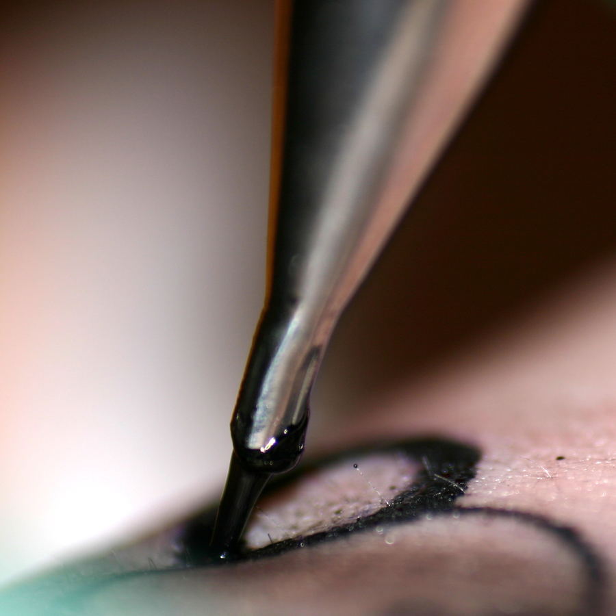 An extreme close-up of a needle laying a black line into skin, with ink pooled at the point.