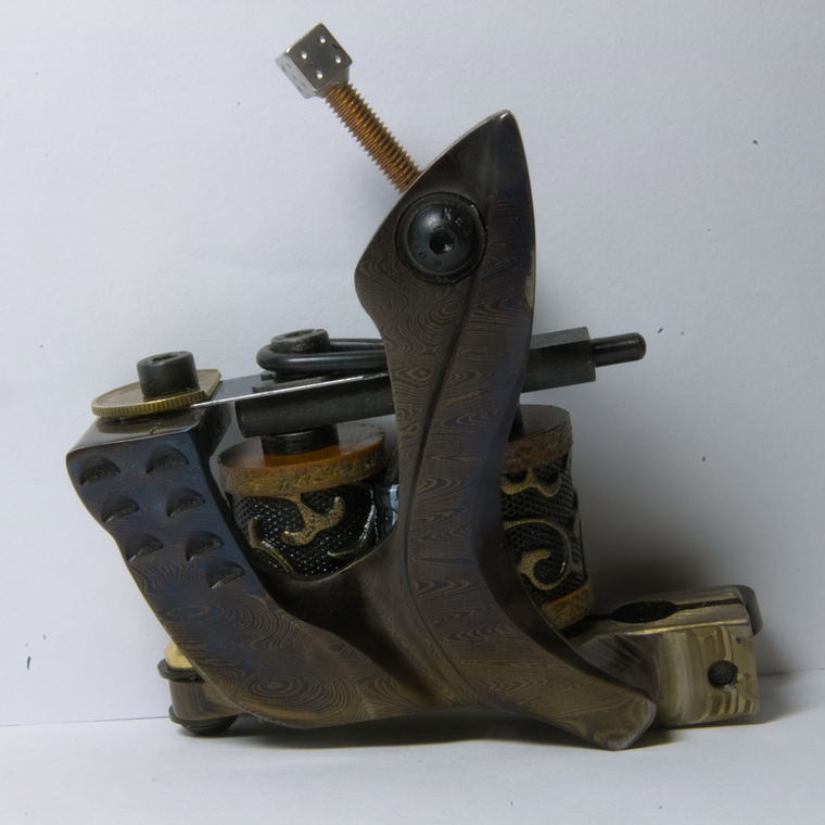 A coil tattoo machine photographed three-quarter on a plain white ground, its frame and springs in full view.