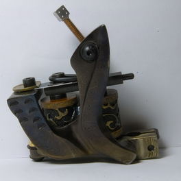 Studio detail: an engraved coil tattoo machine on a plain white ground.