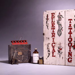 Studio detail: a painted tattooist's case standing open, with a machine and ink bottles inside.